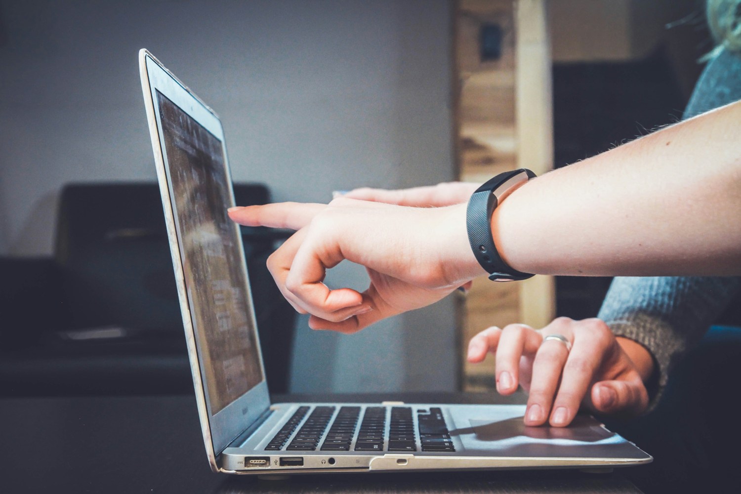 Hands pointing at a laptop while another person works.