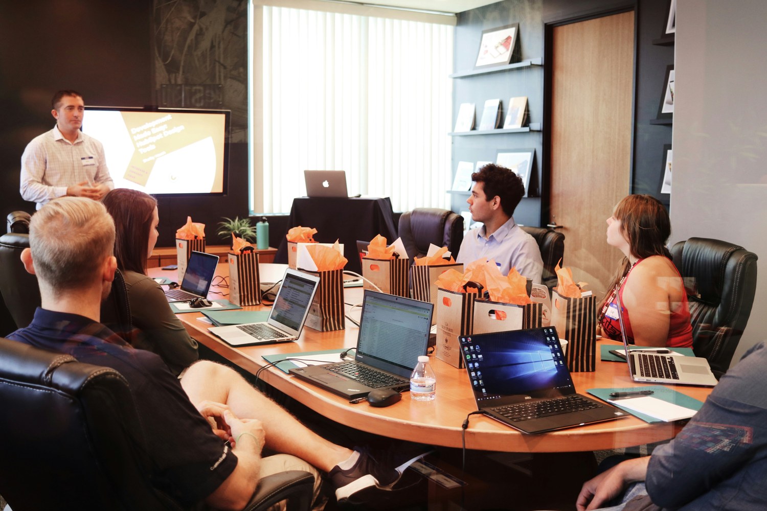 A presenter speaking to a small group around a table with laptops.
